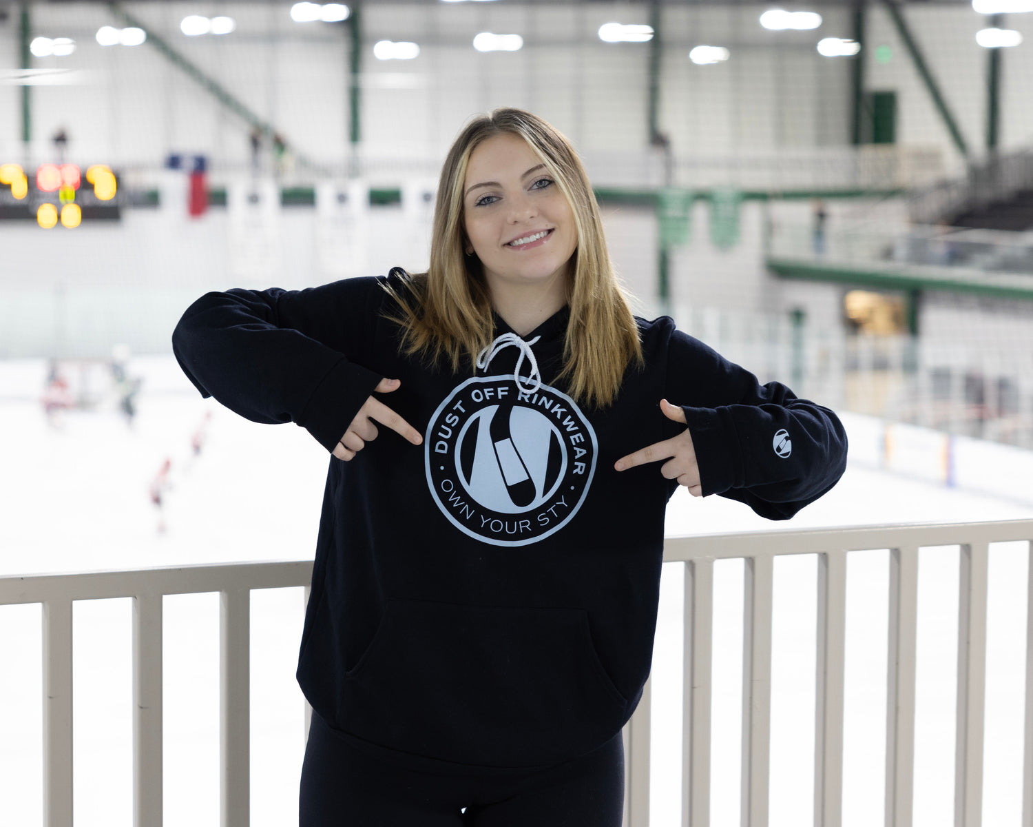 An image of London pointing to her round Dust Off Rinkwear round logo hoodie 