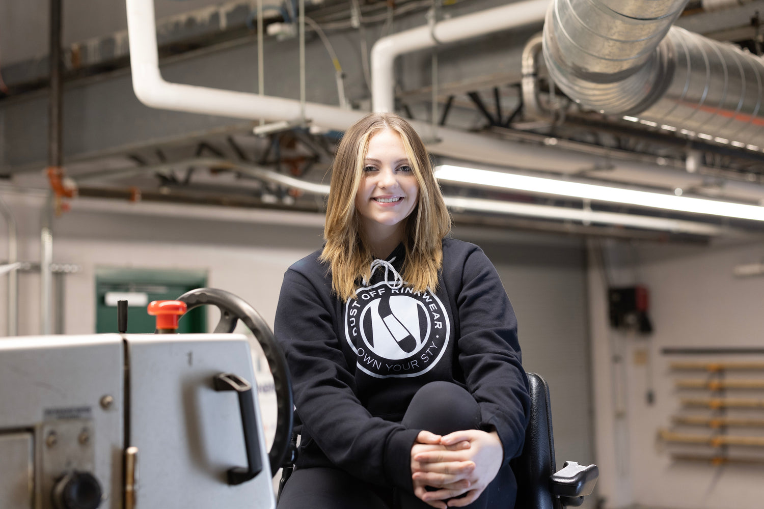 An image of London sitting on a Zamboni in her Dust Off Rinkwear hoodie 